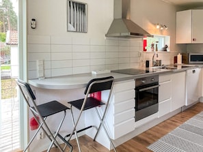 A modern kitchen with white cabinets, a stainless steel range hood, a built-in oven, and a large island with bar stools. - 5 Person Holiday Home in 38472 (Timmernabben)
