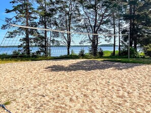 A sandy beach volleyball court with a net, surrounded by trees and a view of a lake. - 5 Person Holiday Home in 38472 (Timmernabben)