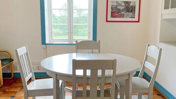 A dining area with a round table and four chairs, a window with curtains, and a framed picture on the wall.