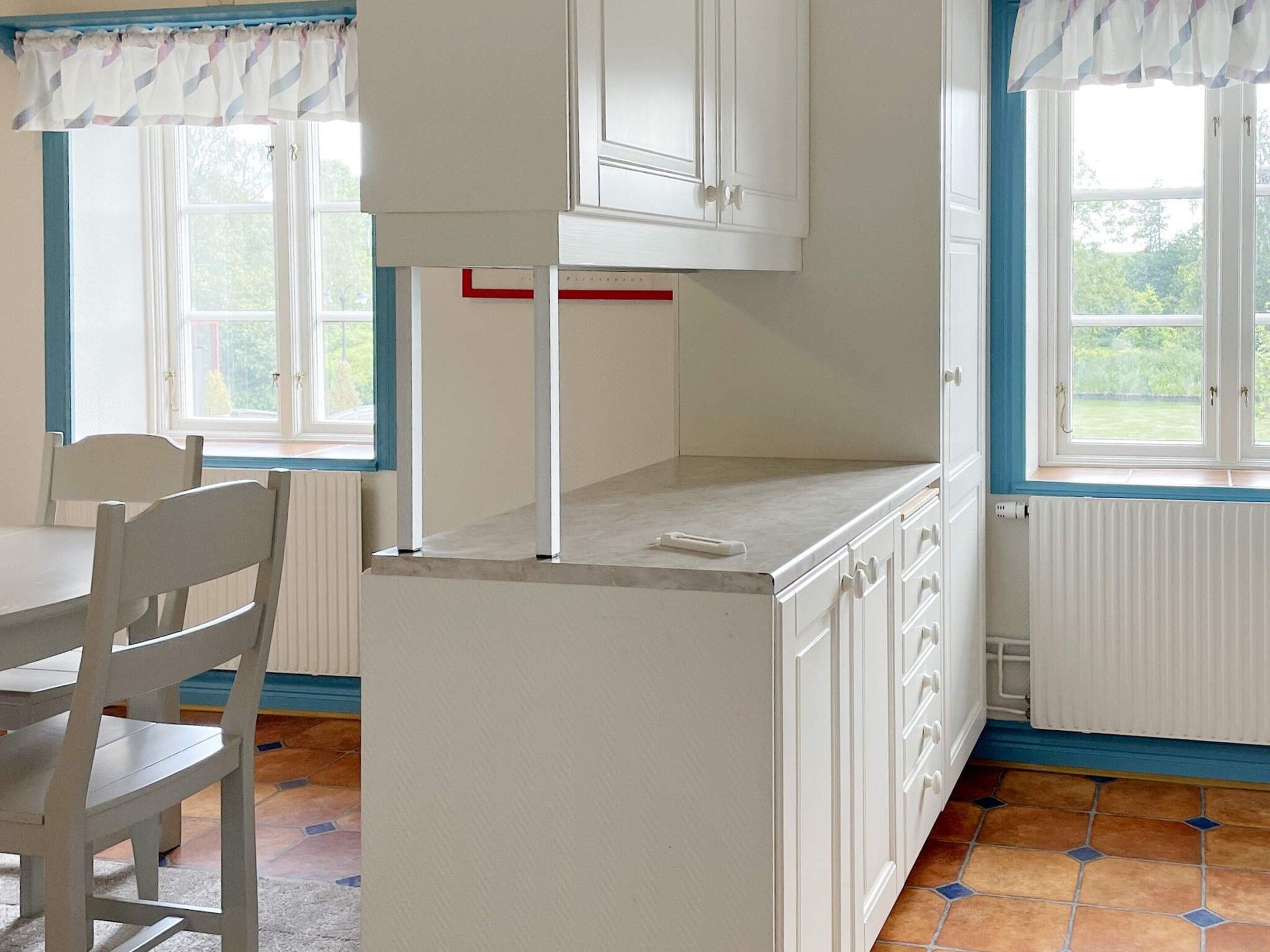Quarto com um armário branco, uma mesa e cadeiras. Há janelas com cortinas.