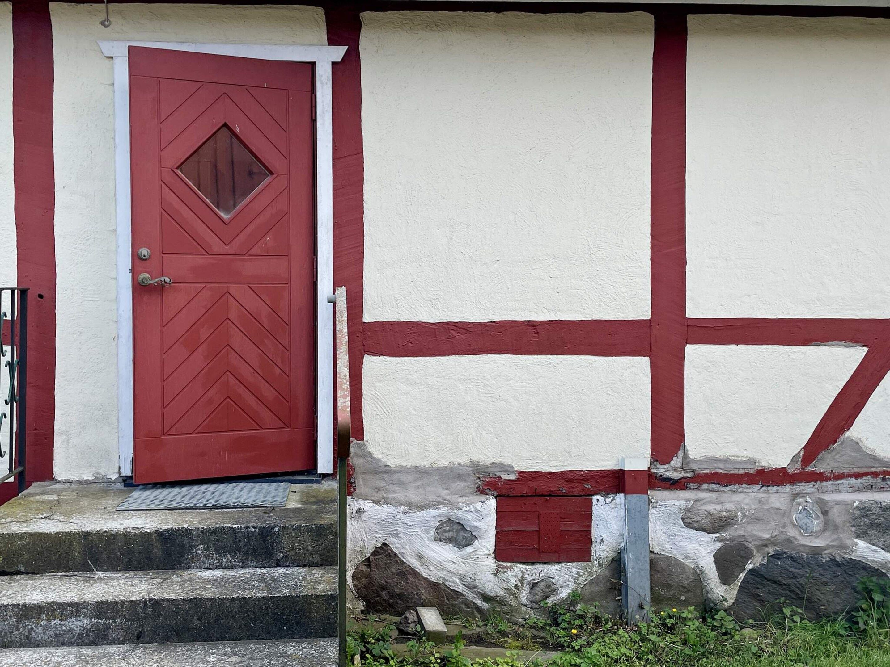 A red door with a diamond-shaped window and a white wall with red trim.
