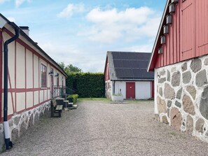 A courtyard with a gravel path, a red building with a stone facade, and a white building with a dark roof. - 4 Person Holiday Home in Lovestad (Lövestad)
