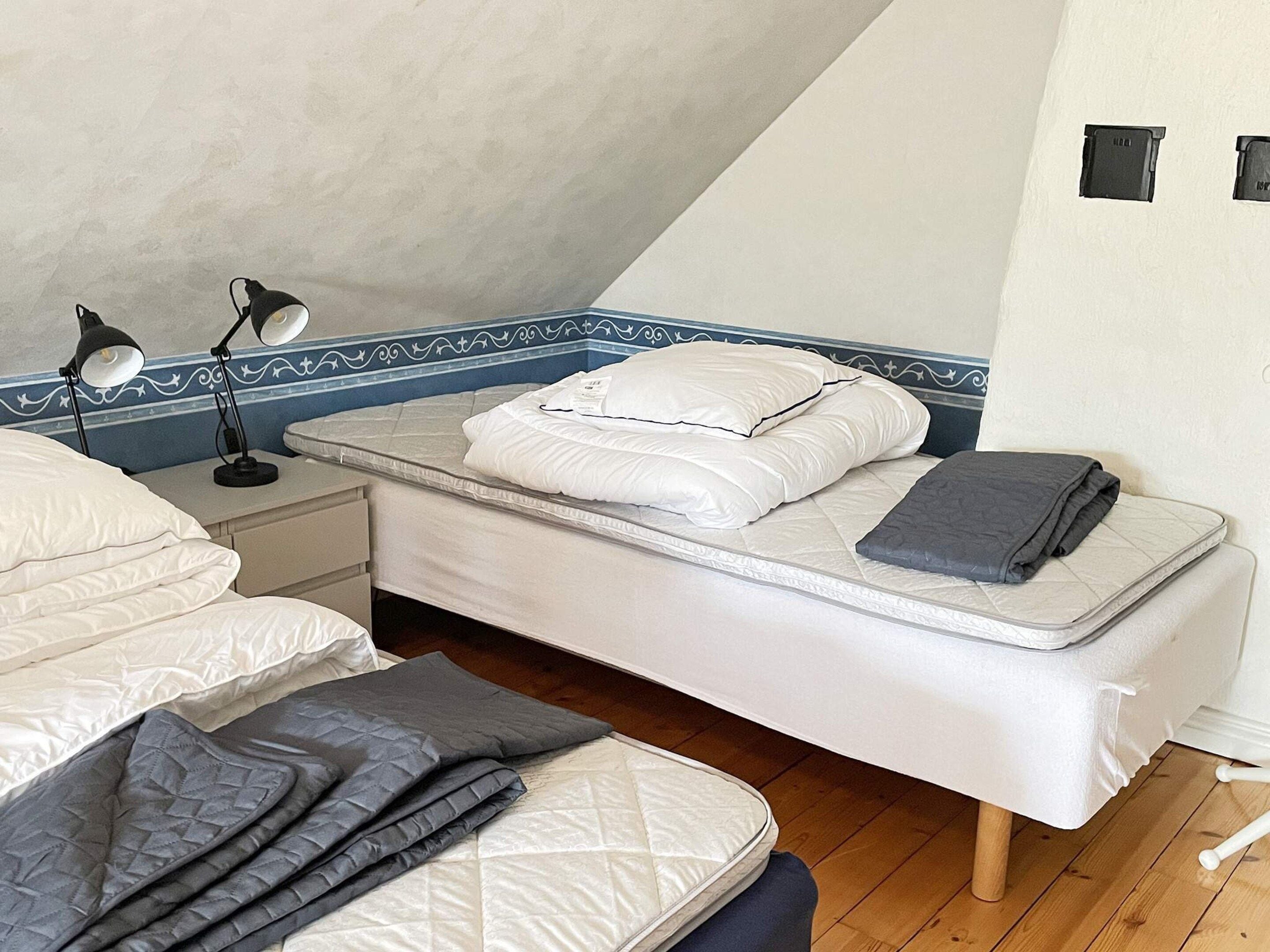 Un dormitorio con una cama individual, una mesita de noche, dos lámparas de noche y un borde decorativo azul en la pared.