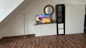 Ett rum med ett sluttande tak, en tv-apparat placerad på ett vitt skåp, ett trägolv och en garderob med en spegel.