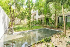 Relax amidst lush greenery and a serene water feature, surrounded by palm trees and modern architecture.