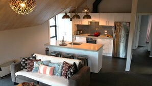 A modern living room with a sofa, coffee table, and a kitchen area with a central island, stove, and refrigerator. - Royale on Cheese (Castle Hill)