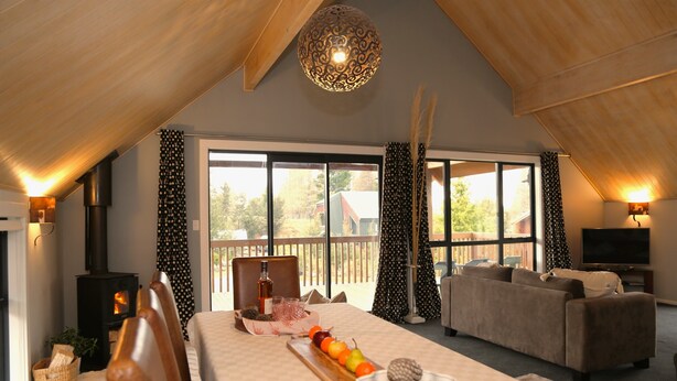 A cozy room with a fireplace, a dining table with fruit and pinecones, a sofa, and large windows. - Royale on Cheese (Castle Hill)