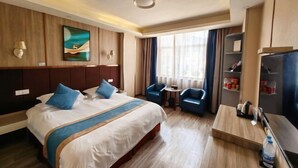 Une chambre d’hôtel avec un grand lit, deux fauteuils, une petite table, un téléviseur et un tableau au mur.