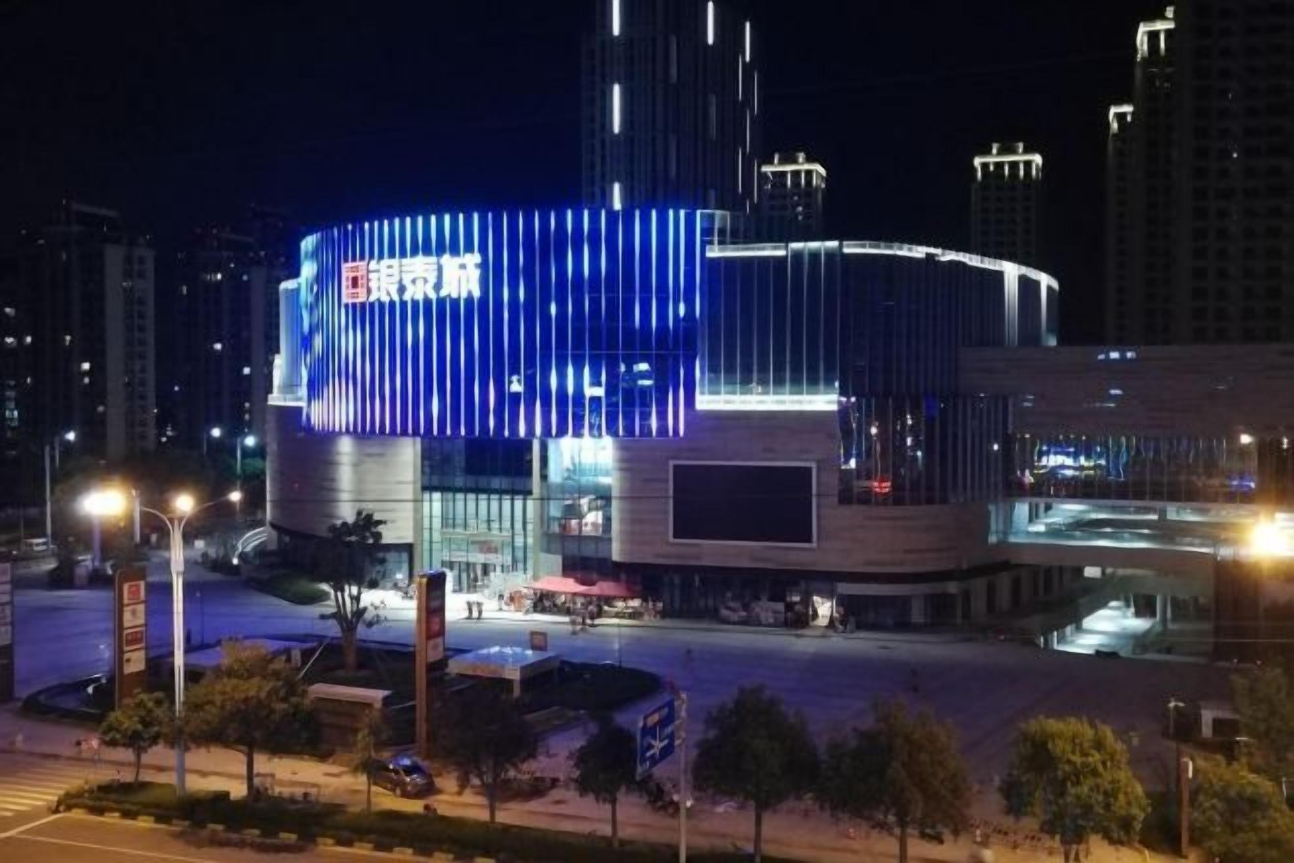 A modern building with a curved facade and illuminated signage, surrounded by a cityscape at night.