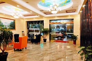 En hotellobby med en receptionsdisk, en sittgrupp och ett stort fönster med utsikt över en bil.