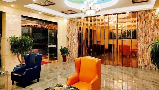 Un hall d’entrée avec un fauteuil bleu, un fauteuil orange, un lustre et une grande fresque au plafond.