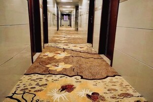 A hallway with a patterned carpet and a view into a room.