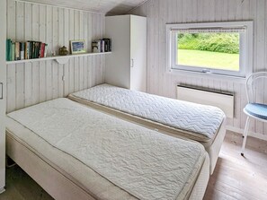 A room with two beds, a window with a view of greenery, a bookshelf with books and a picture frame, and a chair. - 6 Person Holiday Home in Otterup (Otterup)