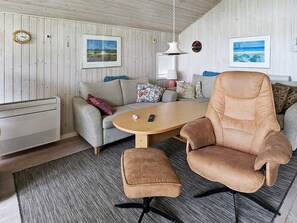 A room with a sofa, armchair, ottoman, and a table. There are two framed pictures on the wall, a clock, and a lamp. - 6 Person Holiday Home in Otterup (Otterup)
