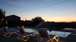 Une piscine avec des chaises longues et un coucher de soleil en arrière-plan.