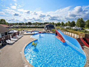 Una gran piscina al aire libre con tobogán, sillas de descanso y una zona cubierta.
