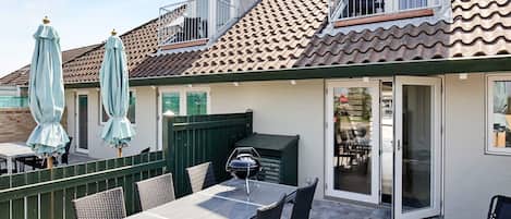A patio area with a table and chairs, a barbecue grill, and umbrellas.