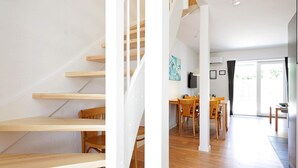 Un intérieur moderne avec un escalier en bois, un coin repas avec des chaises en bois et un téléviseur à écran plat fixé au mur.
