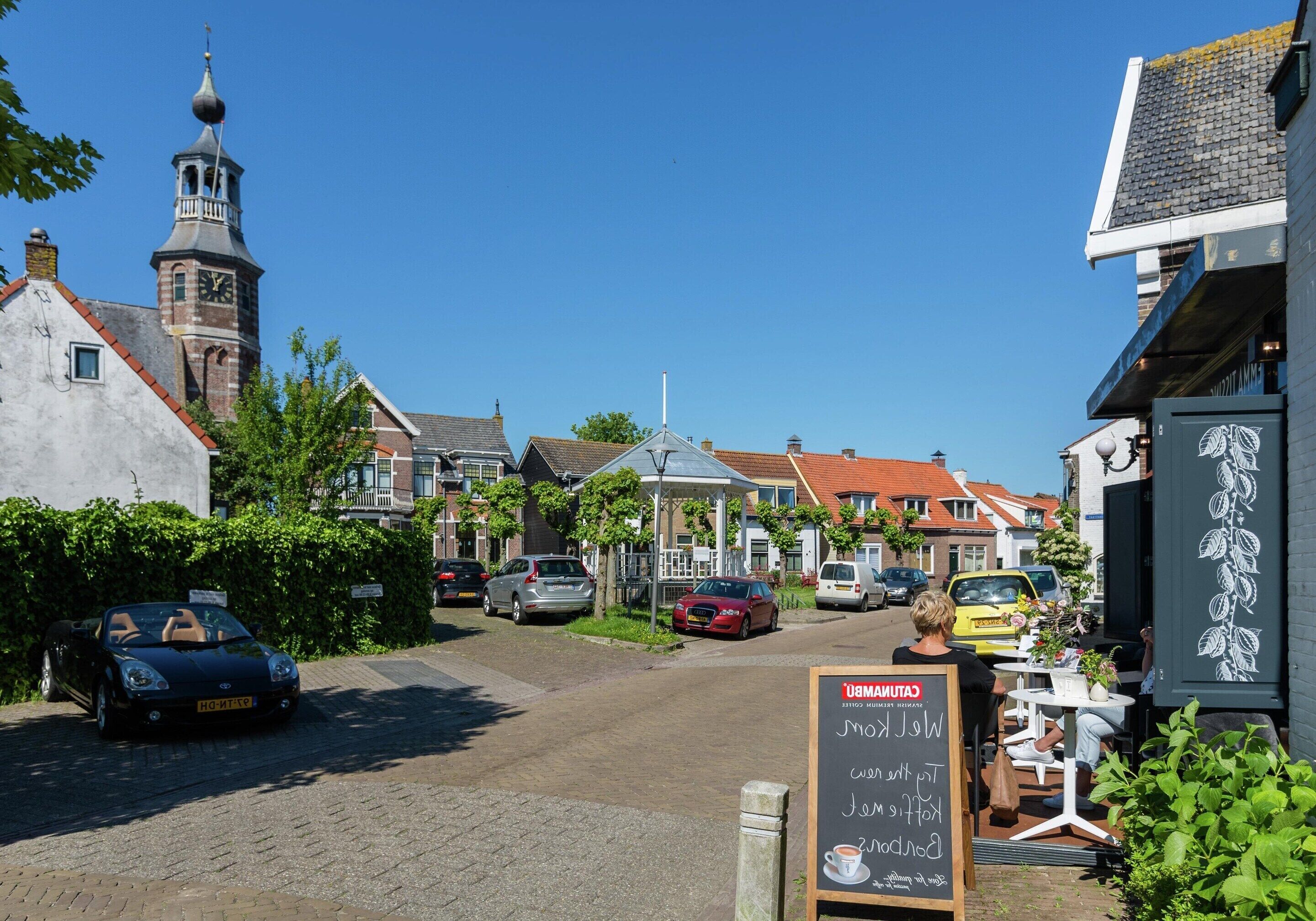 A street view with parked cars, a café with outdoor seating, and traditional buildings with a church tower.