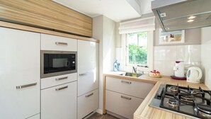 Une cuisine moderne avec des meubles blancs, un four encastré, une cuisinière à gaz et une fenêtre qui laisse entrer la lumière naturelle.