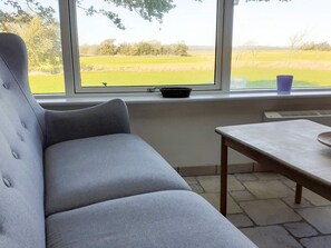 A room with a grey sofa, a small table, and a window with a view of a green field. - 4 Person Holiday Home in Hurup Thy (Hurup Thy)