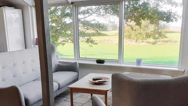 Una sala de estar moderna con un sofá gris, una mesa de centro de madera y un ventanal que ofrece vistas a un paisaje verde.