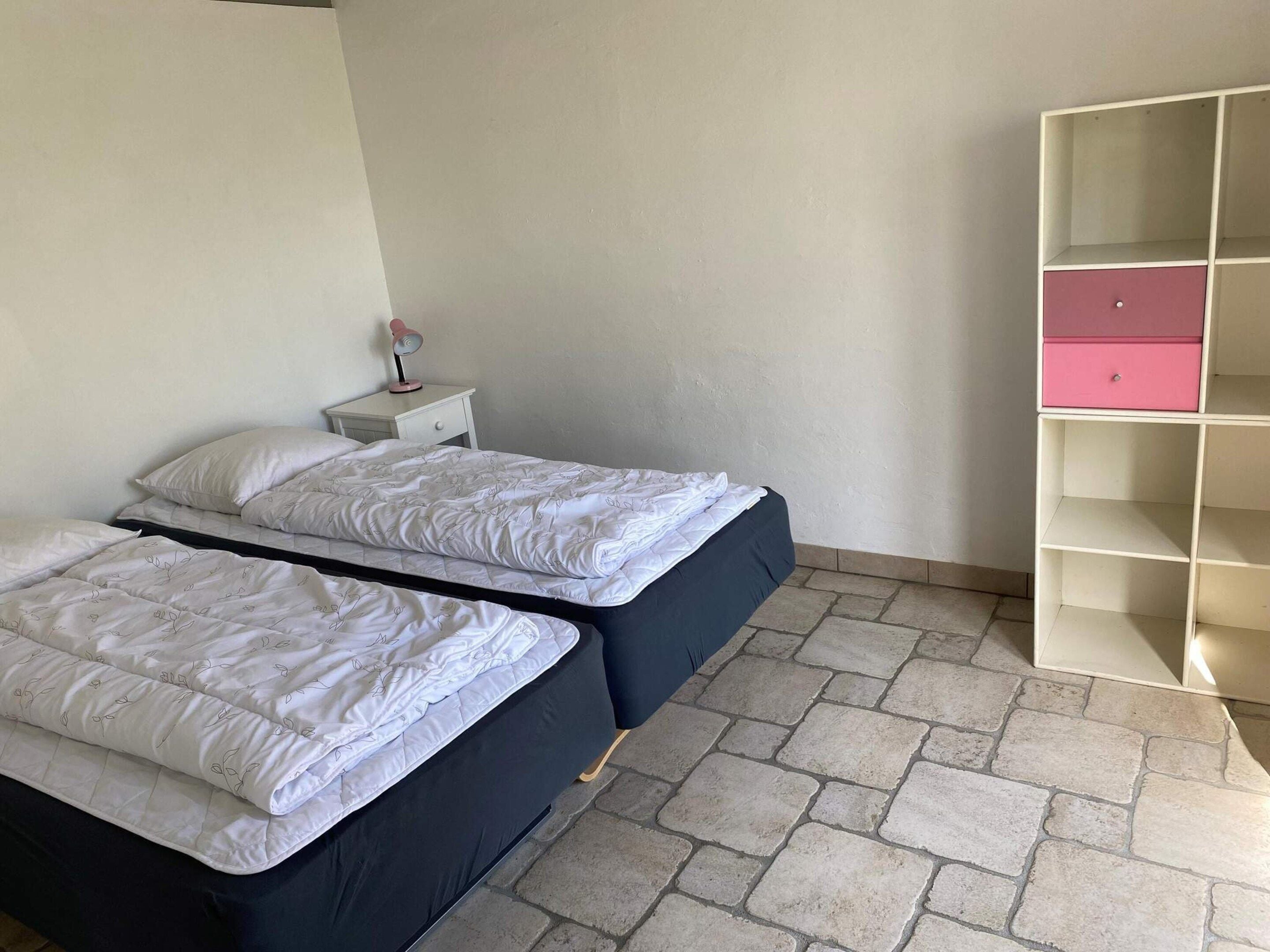 A bedroom with two beds, a nightstand with a lamp, and a pink storage unit.
