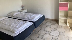 Un dormitorio con dos camas, una mesita de noche con lámpara y un mueble de almacenamiento rosa.