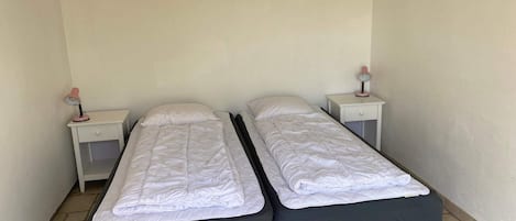 A small, clean room with two single beds, each with a nightstand and a lamp.