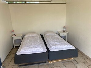 Una habitación pequeña y limpia con dos camas individuales, cada una con una mesita de noche y una lámpara.