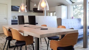 Una cocina moderna con zona de comedor, que incluye una mesa grande, sillas, luces colgantes y un sofá.