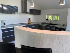 A modern kitchen with a central island, built-in appliances, and pendant lighting. - Light-filled Retreat in Boddum (Hurup Thy)