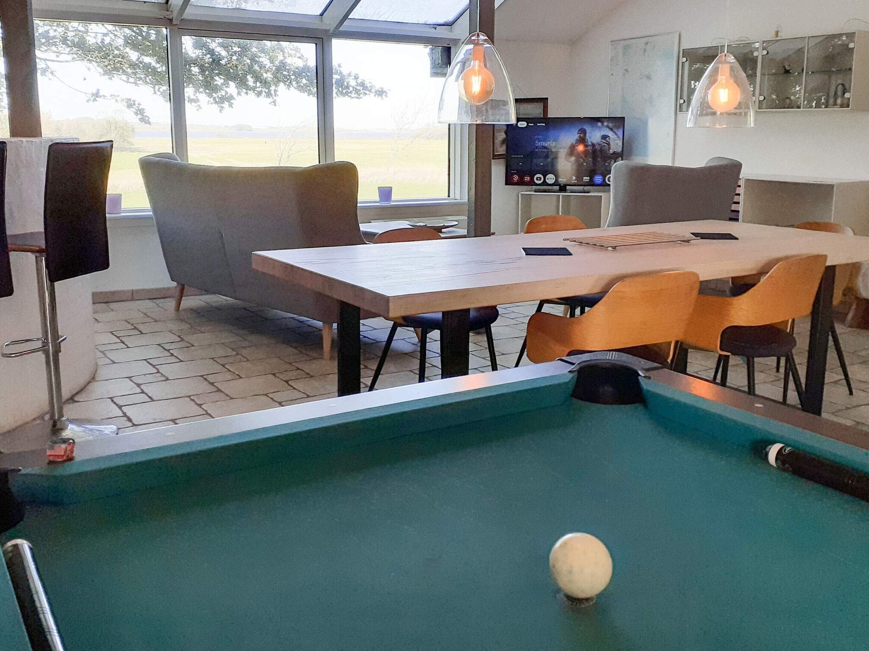 A pool table with a cue ball, surrounded by modern chairs and a dining table.