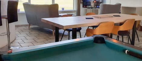 Una mesa de billar con una bola blanca, rodeada de sillas modernas y una mesa de comedor.