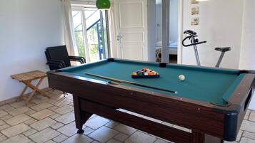 A pool table with a cue stick, a small folding chair, and a pool table cover.