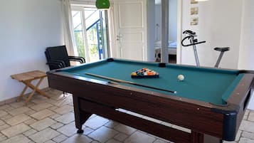 A pool table with a cue stick, a small seating area, and a door leading to another room.