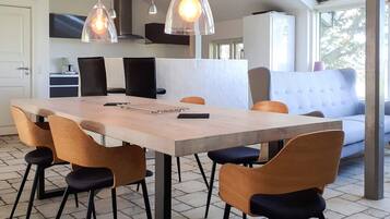 Una cocina moderna con comedor, que incluye una mesa larga, sillas, luces colgantes y un sofá.