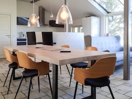 Una cocina moderna con comedor, que incluye una mesa larga, sillas, luces colgantes y un sofá.