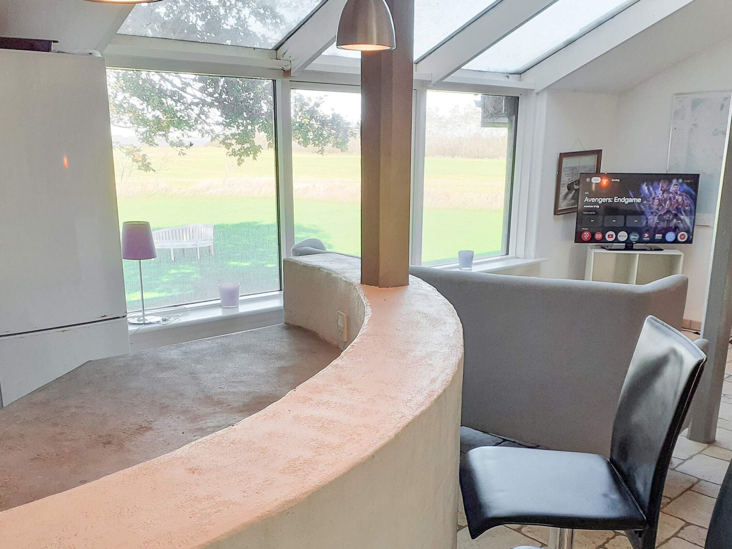 A modern kitchen with a curved countertop, a built-in oven, and a large window offering a view of a green landscape.