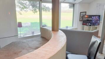 A modern kitchen with a curved countertop, a built-in oven, and a large window offering a view of a green landscape.