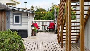 Eine Holzterrasse mit überdachter Sitzgruppe, einem kleinen Tisch und einem Blumentopf.