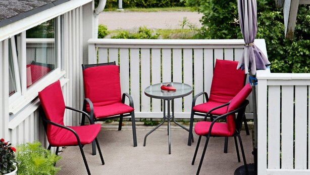 Un balcon avec deux chaises rouges, une petite table ronde et une clôture blanche.