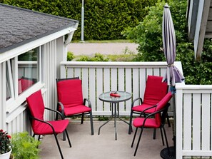 Ein Balkon mit zwei roten Stühlen, einem kleinen runden Tisch und einem weißen Geländer.