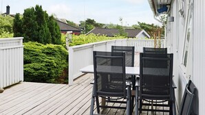 Eine Holzterrasse mit einem weißen Zaun, zwei schwarzen Stühlen und einem Tisch.