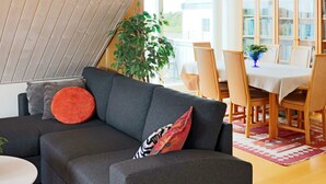 Un salon moderne avec un canapé gris foncé, une petite table d’appoint blanche et un coin repas comprenant des chaises et une table en bois.