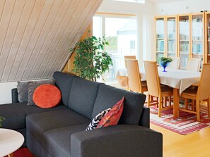 A modern living room with a dark grey sofa, a small white side table, and a dining area with wooden chairs and a table. - 4 Star Holiday Home in Frillesas (Frillesas)