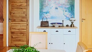Un coin repas comprenant une table, des chaises, un bol bleu avec des plantes vertes, un meuble blanc avec des tiroirs et un tableau accroché au mur.
