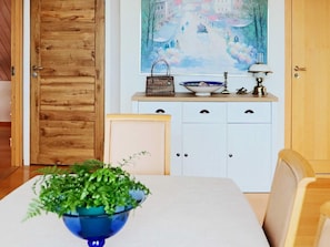 A dining area with a table, chairs, a blue bowl with green plants, a white cabinet with drawers, and a painting on the wall. - 4 Star Holiday Home in Frillesas (Frillesas)