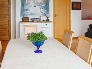 Een eettafel met een blauwe glazen schaal met groene planten, een witte tafelkleed en houten stoelen.