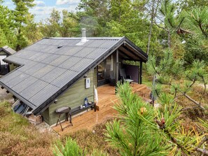 En hytte med skråtag, træterrasse og overdækket udendørs siddeplads.